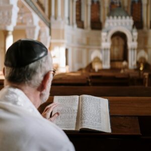 A man wearing a kippah reads religious texts inside a beautifully ornate synagogue.
